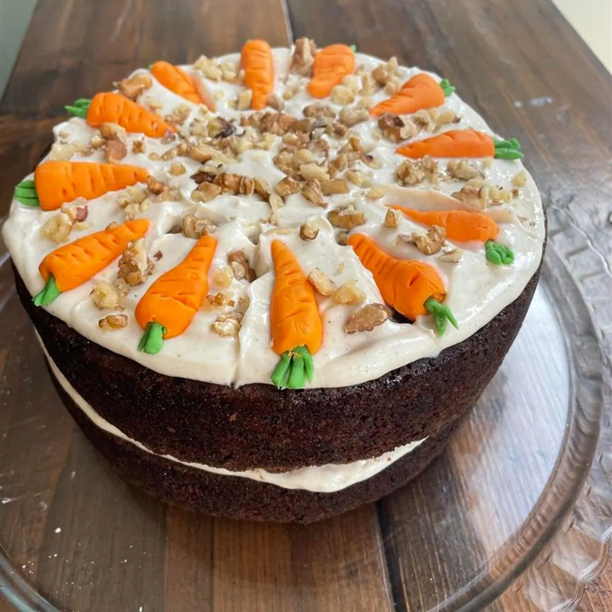 Two-layer carrot cake with cream cheese frosting, chopped nuts and little icing carrots